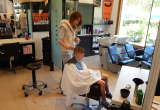 En dreng får klippet hår af en frisør i en moderne salon ved Camping Pra'delle Torri i Veneto, Italien.