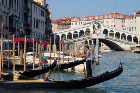 Gondolier rowing along the Grand Canal with the iconic Rialto Bridge in the background in Venice, Italy.