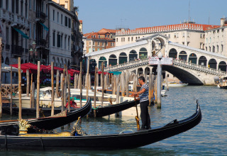 Gondolier rowing along the Grand Canal with the iconic Rialto Bridge in the background in Venice, Italy.