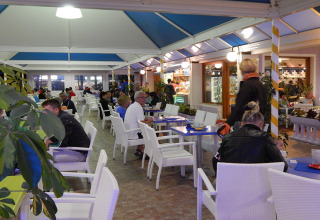 Guests enjoy a meal in a covered outdoor dining area at Camping Pra'delle Torri in Veneto, Italy.