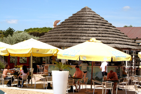 Café al aire libre con huéspedes bajo sombrillas amarillas en Camping Pra'delle Torri, Véneto, Italia.
