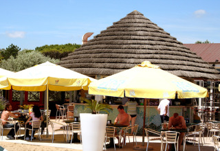 Udendørs café med gæster under gule parasoller ved Camping Pra'delle Torri-feriepark i Veneto, Italien.