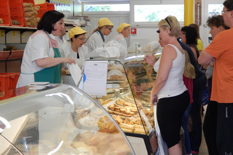 Clienti in fila in una panetteria al Camping Pra'delle Torri in Veneto, Italia, serviti dal personale.
