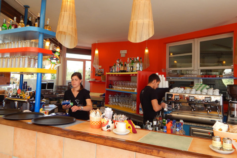 Dos empleados trabajan detrás de la barra en Camping Pra'delle Torri, Véneto, Italia, con decoración colorida.