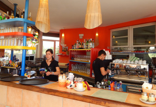 Due membri dello staff lavorano dietro il bancone al Camping Pra'delle Torri in Veneto, Italia, con arredi colorati.