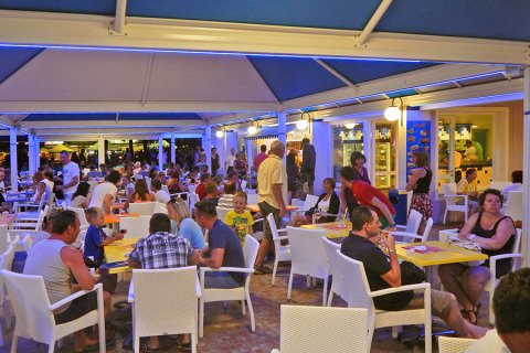 Restaurante al aire libre en Camping Pra'delle Torri, Veneto, Italia, lleno de huéspedes en una noche animada.