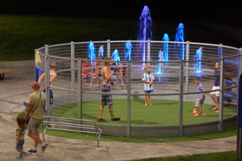 Children play football in a fenced playground at night at Camping Pra'delle Torri, Veneto, Italy.