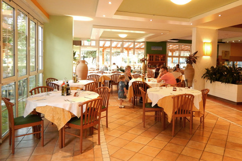 Restaurante en Camping Pra'delle Torri, Véneto, Italia, con mesas puestas, sillas de madera y comensales.