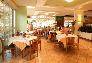 Restaurant op Camping Pra'delle Torri, Veneto, Italië met gedekte tafels, houten stoelen en etende mensen.