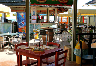 Cafetería al aire libre en Camping Pra'delle Torri, Véneto, Italia, con mesas, sillas y sombrillas visibles.