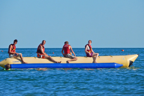 Quattro persone su una banana boat gonfiabile nel mare del Camping Pra'delle Torri, villaggio vacanze in Veneto, Italia.