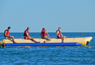 Four people riding an inflatable banana boat at sea in Camping Pra'delle Torri holiday park, Veneto, Italy.
