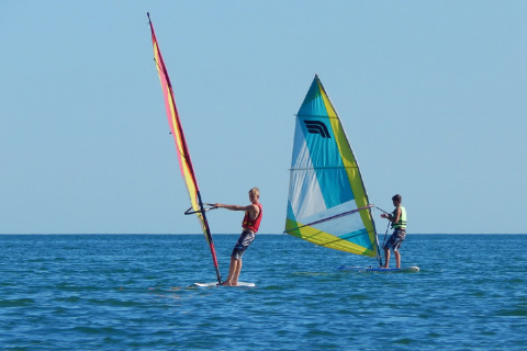 Two people windsurfing on the sea near Camping Pra'delle Torri, a holiday park in Veneto, Italy, under clear sky.