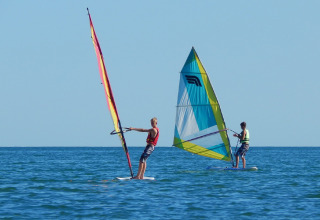 Two people windsurfing on the sea near Camping Pra'delle Torri, a holiday park in Veneto, Italy, under clear sky.