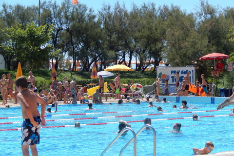 People enjoying the outdoor pool at Camping Pra'delle Torri holiday park in Veneto, Italy on a sunny day.