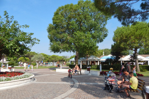 Vakantiegangers ontspannen op zonnig plein in Camping Pra'delle Torri, Veneto, Italië, tussen bloemen en bomen.
