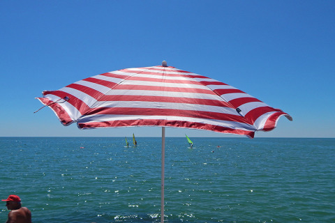 En rød og hvid stribet parasol på Camping Pra'delle Torri med udsigt over havet i Veneto, Italien.
