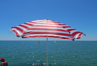 En rød og hvid stribet parasol på Camping Pra'delle Torri med udsigt over havet i Veneto, Italien.