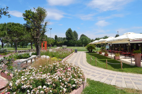 Sentiero nel giardino con fiori, alberi e ristorante all'aperto al Camping Pra'delle Torri, Veneto, Italia.