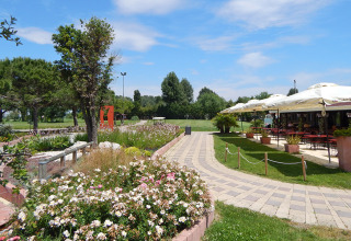 Hyggelig sti i en have med blomster, træer og udendørs restaurant på Camping Pra'delle Torri i Veneto, Italien.