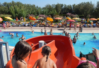 Children preparing to go down a red waterslide at a busy pool in Camping Pra'delle Torri, Veneto, Italy.
