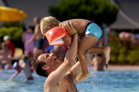Un padre levanta feliz a su hijo en la piscina del Camping Pra'delle Torri, un parque vacacional en Véneto, Italia.