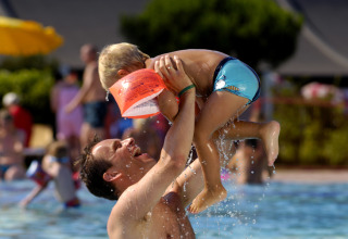 A father joyfully lifts his child in the swimming pool at Camping Pra'delle Torri holiday park in Veneto, Italy.