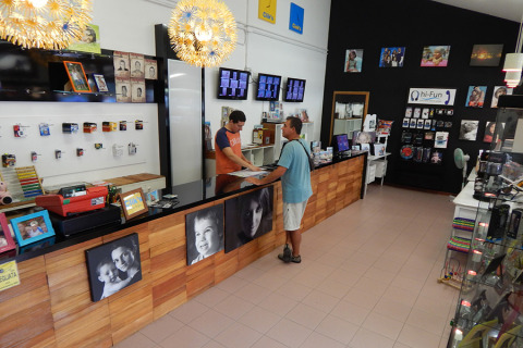 Interior de una tienda de fotos y electrónica en Camping Pra'delle Torri, Véneto, Italia, con dos personas en el mostrador.
