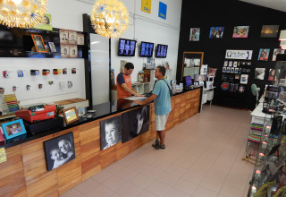 Interno di un negozio di foto ed elettronica al Camping Pra'delle Torri, Veneto, Italia, con due persone al bancone.