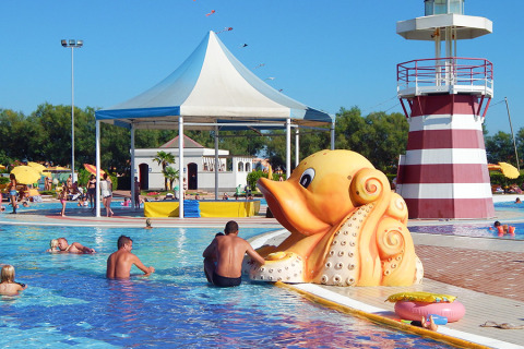 Familias disfrutan piscina infantil con gran figura de pulpo y faro en Camping Pra'delle Torri, Véneto.