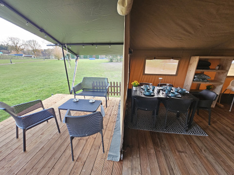 Safari tent with covered terrace and dining area at The HappyFarm in the Netherlands, overlooking grass.