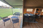 Safari tent with covered terrace and dining area at The HappyFarm in the Netherlands, overlooking grass.