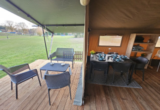 Safari tent with covered terrace and dining area at The HappyFarm in the Netherlands, overlooking grass.