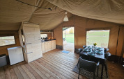 Interno di una tenda safari con pavimento in legno, tavolo da pranzo e cucina a HappyFarm, Olanda.