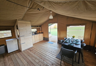 Interior view of a safari tent with wooden floor, dining table, and kitchen at HappyFarm, Netherlands.