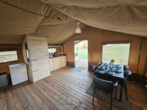 Binnenzicht van een safaritent met houten vloer, eettafel en keuken bij HappyFarm, Nederland.