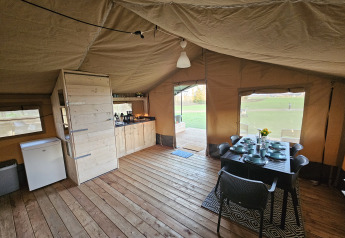 Vista interior de una tienda safari con suelo de madera, mesa de comedor y cocina en HappyFarm, Países Bajos.