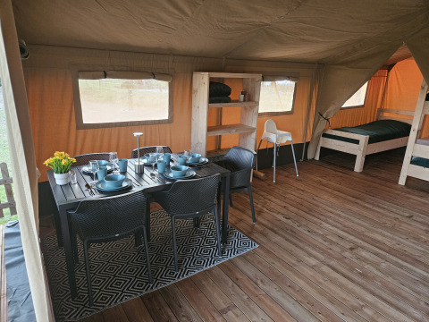 Interieur van safari tent met toilet bij The HappyFarm, Nederland, met eettafel, bedden en houten vloer.