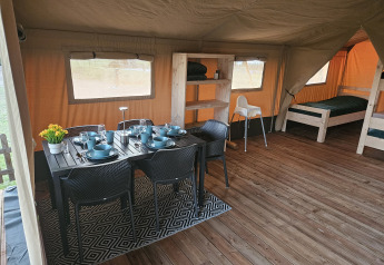 Interno di tenda safari a The HappyFarm, Paesi Bassi, con tavolo da pranzo, letti e pavimento in legno.