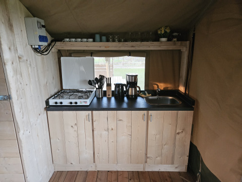Kleine keuken met gasfornuis, gootsteen en koffiezetapparaat in een safaritent bij The HappyFarm in Nederland.