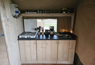 Small kitchen with gas stove, sink, and coffee maker inside a safari tent at The HappyFarm in the Netherlands.