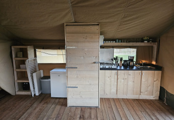 Indretning af et safari-telt med trægulv, tekøkken, hylder og køleskab, HappyFarm, Holland.