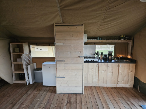 Indretning af et safari-telt med trægulv, tekøkken, hylder og køleskab, HappyFarm, Holland.