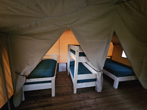 Intérieur tente safari avec quatre lits sur plancher bois à The HappyFarm, aux Pays-Bas, ambiance cosy.
