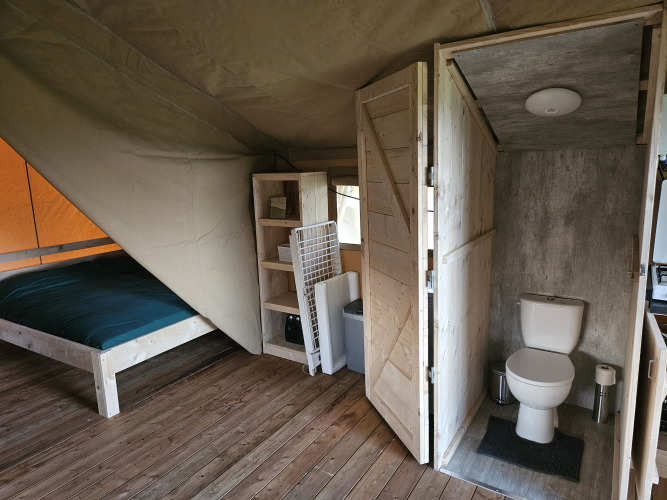 Interieur van een safaritent met houten vloer, bed, rek en privétoilet bij HappyFarm in Nederland.