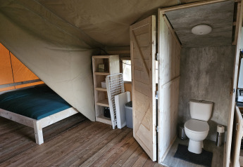 Interior of a safari tent with wooden floor, bed, shelving, and private toilet at HappyFarm in the Netherlands.