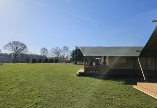 Safaritent met toilet bij The HappyFarm in Nederland, groot grasveld en mensen op het terras in de zon.