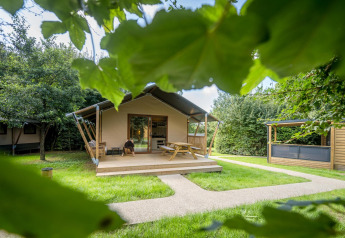 Tienda glamping familiar en Urban-Gardens Ieper, Bélgica, rodeada de césped verde y frondosos árboles.