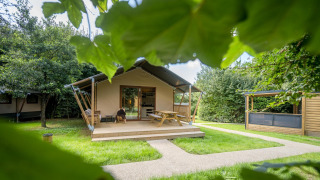 Familie glampingtent aan Urban-Gardens Ieper in België, omgeven door grasvelden en groene bomen.