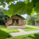 Tienda glamping familiar en Urban-Gardens Ieper, Bélgica, rodeada de césped verde y frondosos árboles.